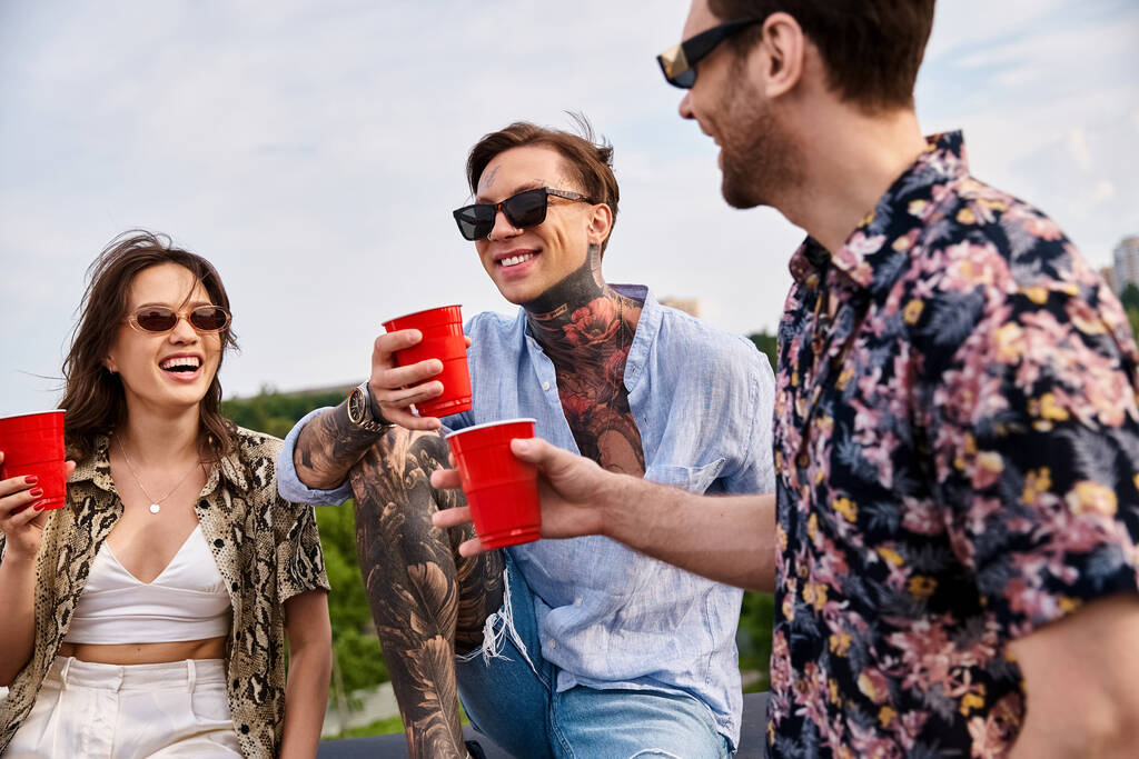 veselé dobře vypadající přátelé v pulzující oblečení cinkání jejich červené poháry s nápoji na střeše - Fotografie, Obrázek