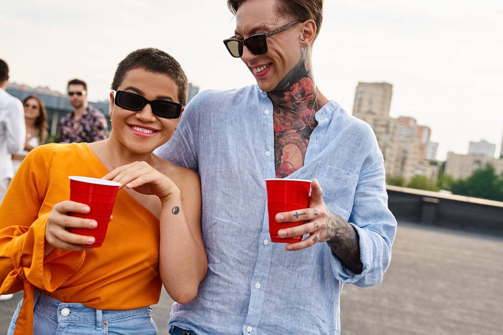 веселые мужчина и женщина с красными чашками глядя друг на друга со своими межрасовыми друзьями на заднем плане - Фото, изображение