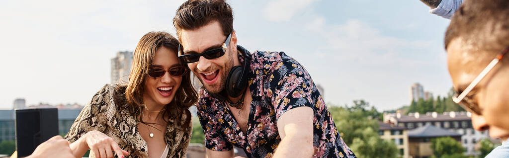 весёлые мультикультурные друзья в модных солнцезащитных очках отлично проводят время на вечеринке на крыше с DJ - Фото, изображение