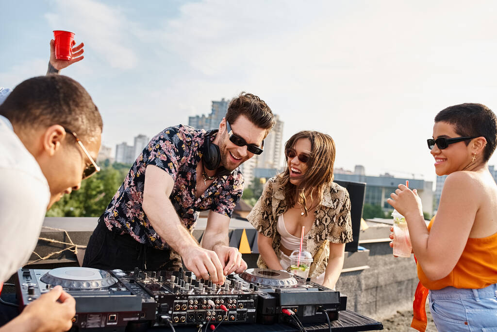 fröhliche multikulturelle Freunde mit stylischer Sonnenbrille feiern auf dem Dach neben DJ-Equipment - Foto, Bild