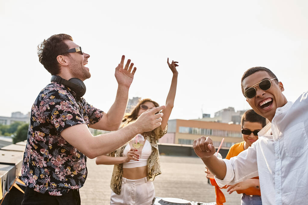 amigos multiculturais alegres com óculos de sol elegantes festa para DJ conjunto no telhado juntos - Foto, Imagem