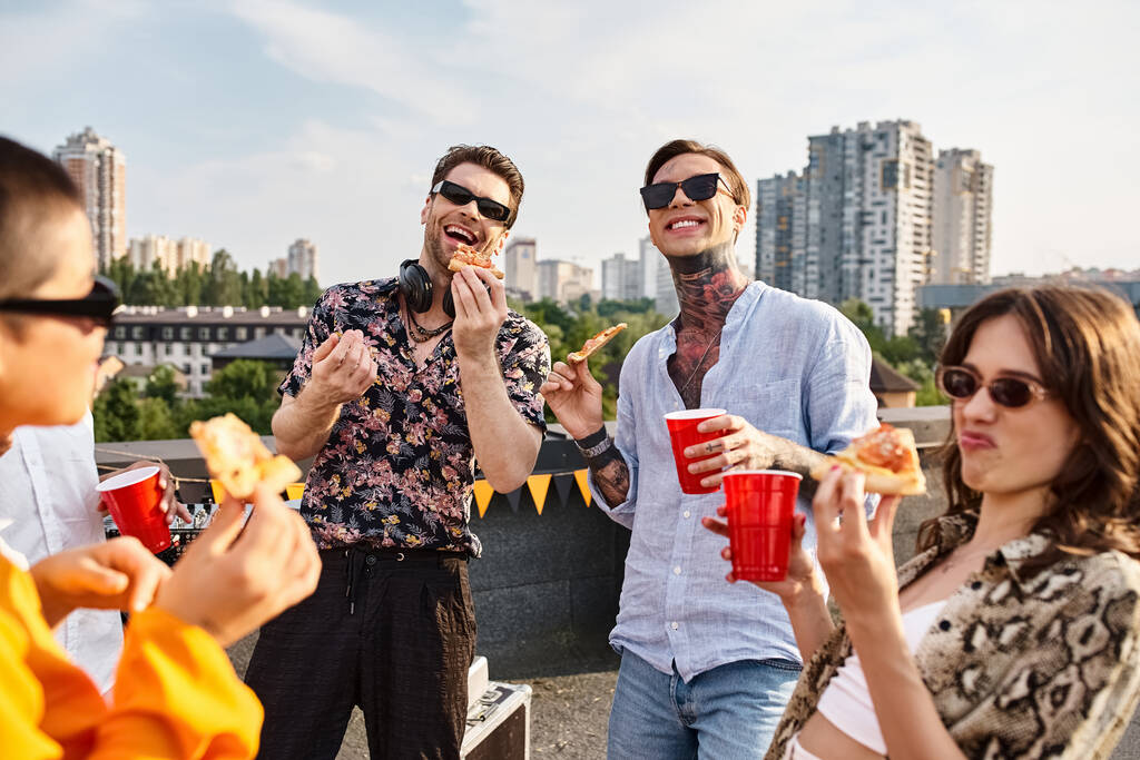 vreugdevolle aantrekkelijke vrienden in stijlvolle stedelijke kleding pizza eten en genieten van drankjes op het feest - Foto, afbeelding