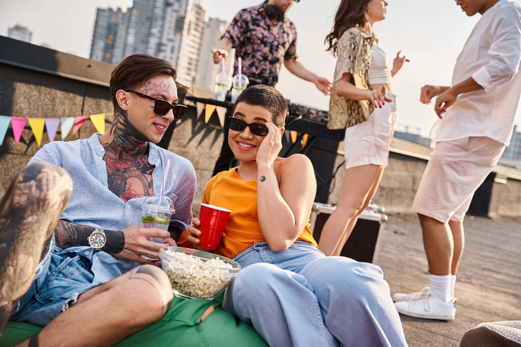 alegres amigos multirraciales disfrutando de cócteles de alcohol en la fiesta en la azotea con DJ en el telón de fondo - Foto, Imagen