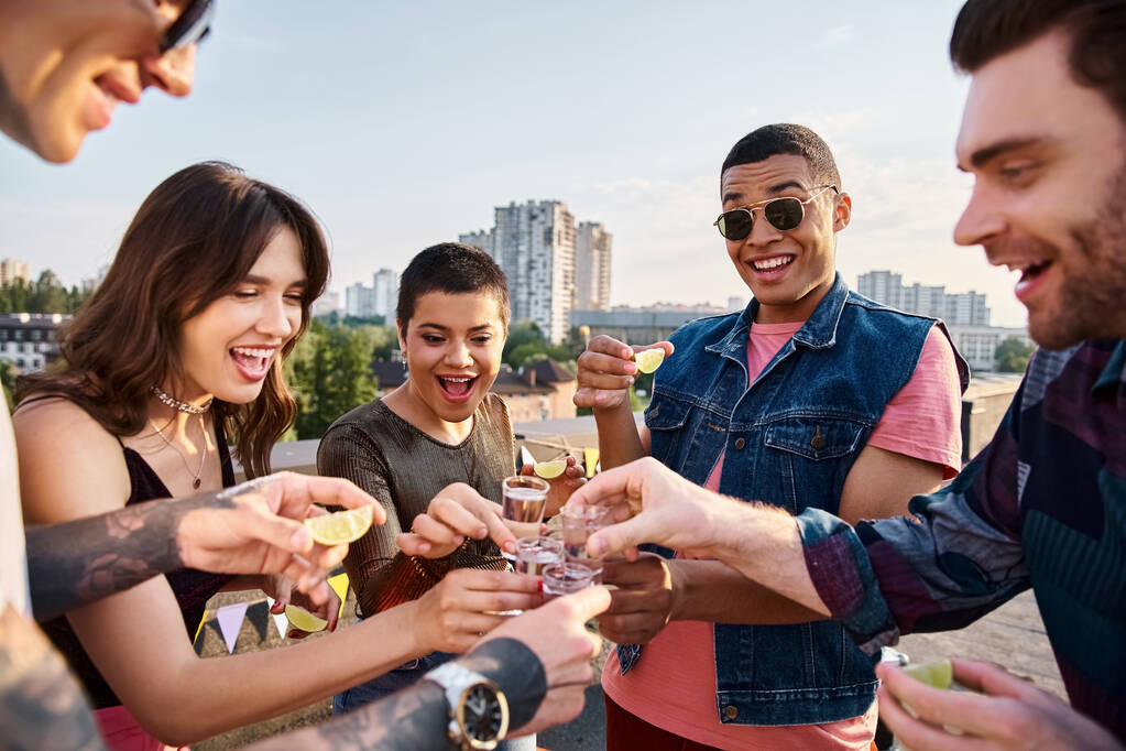 skupina veselých multikulturních přátel pije tequilu s čerstvým vápnem a solí na střešním večírku - Fotografie, Obrázek
