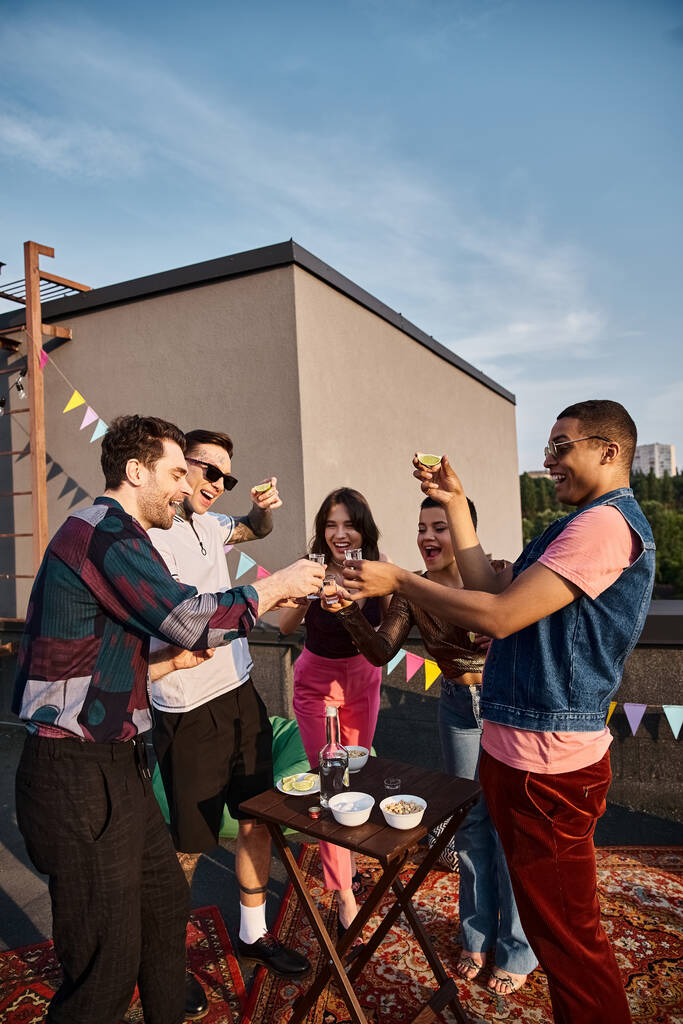 группа веселых мультикультурных друзей, пьющих текилу со свежей лаймом и солью на вечеринке на крыше - Фото, изображение