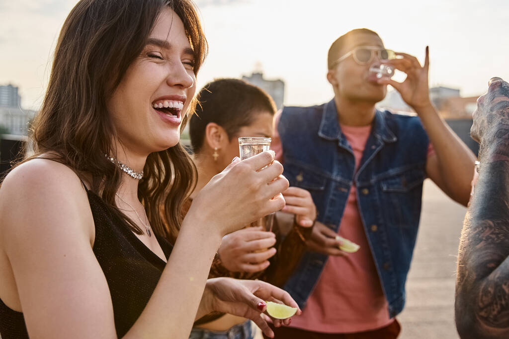 gente multicultural alegre en ropa vibrante disfrutando de tequila con sal y lima en la fiesta en la azotea - Foto, imagen
