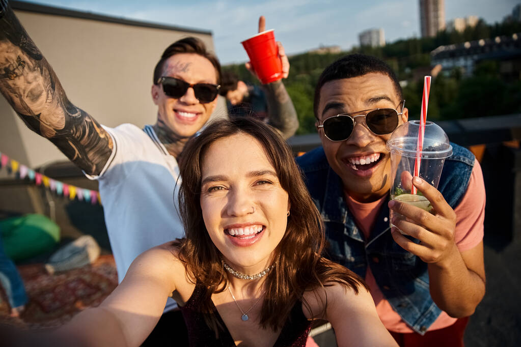 cheerful multicultural friends holding cocktails in hands and having fun at rooftop party - Photo, Image