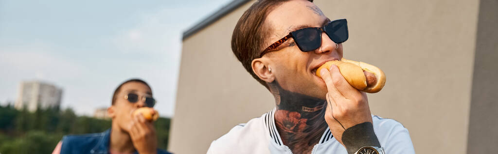 skupienie się na młodym człowieku z tatuażami ze swoim afrykańskim przyjacielem na tle jedzenia hot dogów, baner - Zdjęcie, obraz