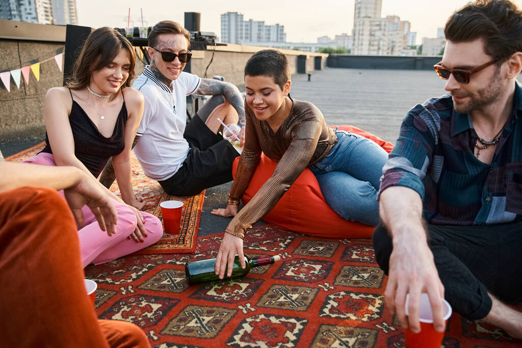 веселые веселые разнообразные друзья в повседневных стильных одеждах, играющие в бутылочку вместе на вечеринке - Фото, изображение
