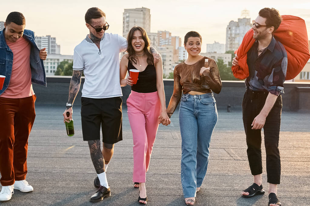 joyous interracial friends with different drinks and bean bag chair in hands at rooftop party - Photo, Image