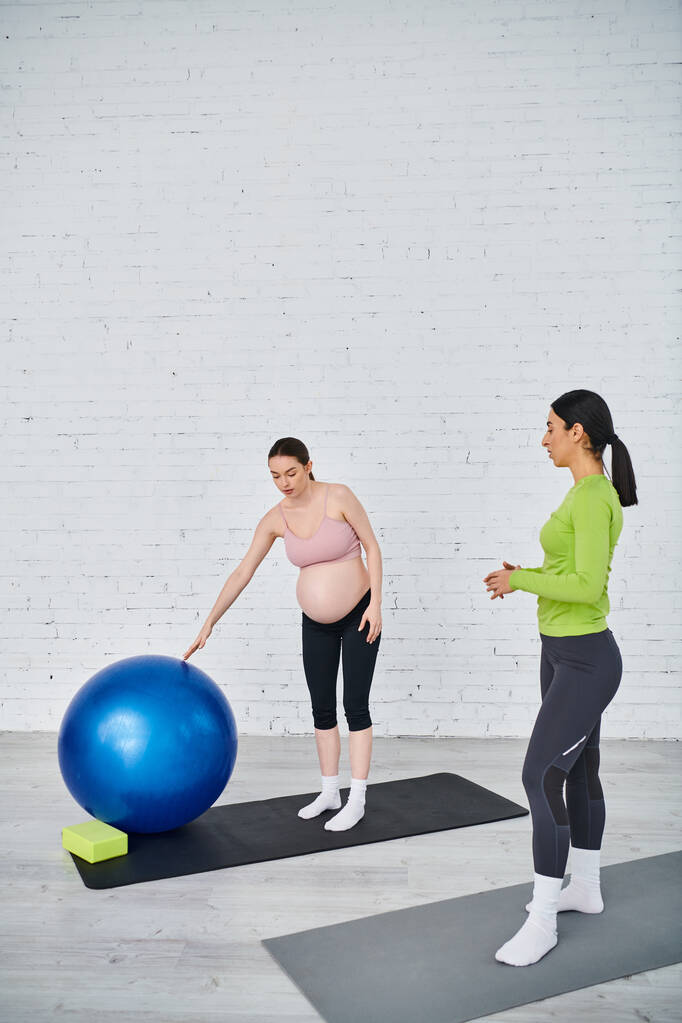 Una donna incinta si trova accanto a una palla da ginnastica blu, praticando l'equilibrio durante una sessione di allenamento del corso dei genitori. - Foto, immagini