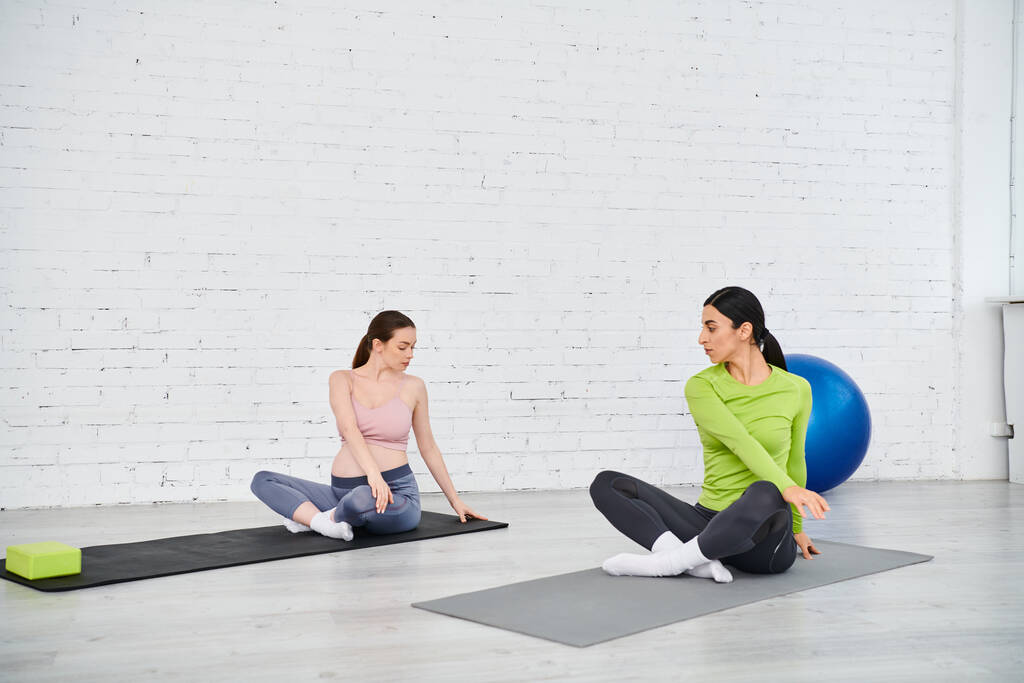 A pregnant woman exercises with her coach during a parents course, sitting on yoga mats in a serene setting. - Photo, Image