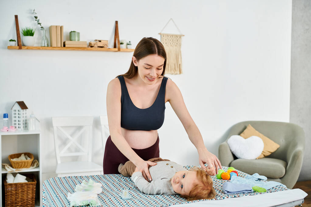 Una madre joven juega alegremente con su bebé en una cama acogedora, guiada por un entrenador experimentado de un curso de padres. - Foto, imagen