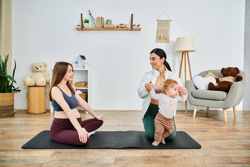 Genç bir anne yoga minderinde oturup, evde ebeveyn kursu sırasında koçtan rehberlik alırken bebeğiyle barışçıl bir şekilde bağ kuruyor.. - Fotoğraf, Görsel