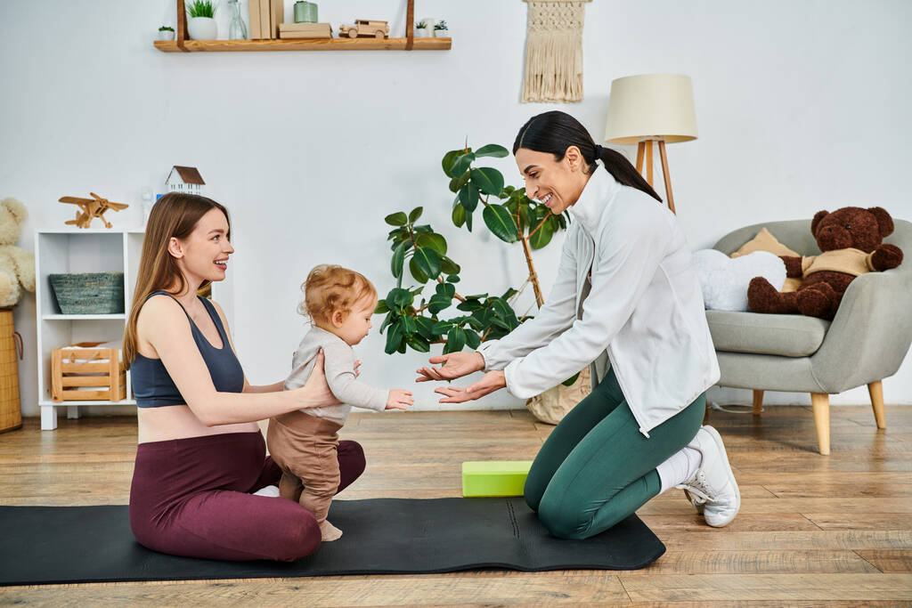 Una giovane bella madre e il suo bambino impegnati in una tranquilla sessione di yoga guidati dal loro istruttore in un corso di genitori. - Foto, immagini