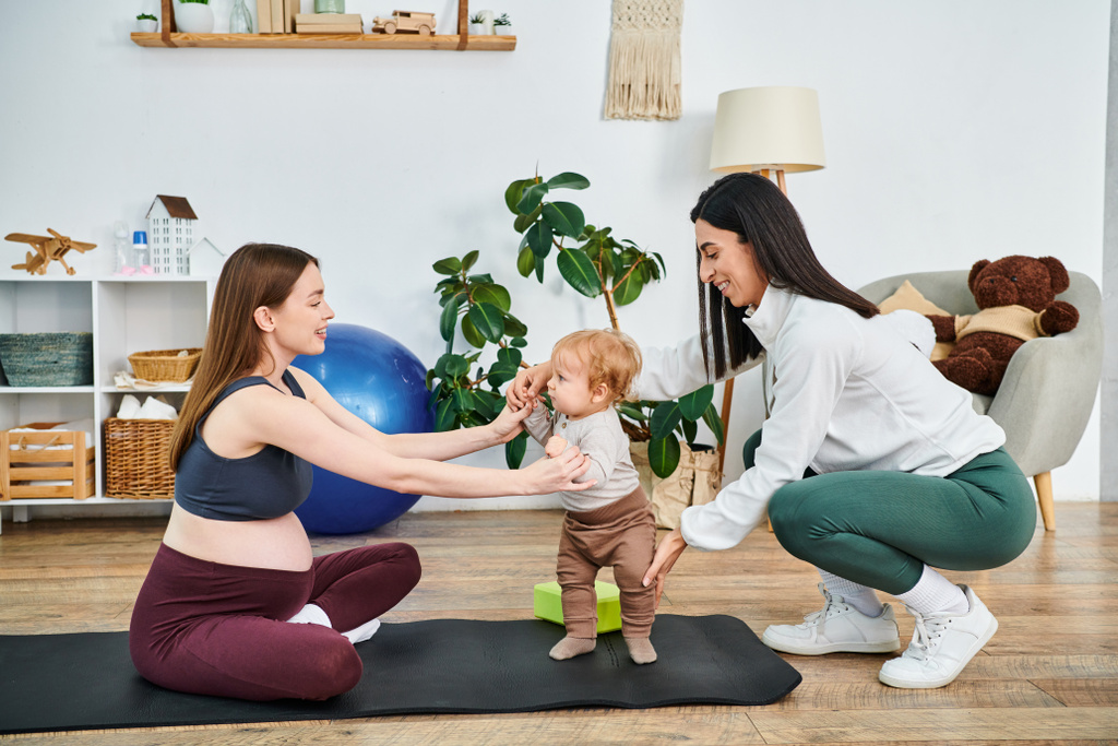 Een jonge mooie moeder bezig met speelse yoga bewegingen met haar baby op een mat, begeleid door een coach bij ouders cursussen. - Foto, afbeelding