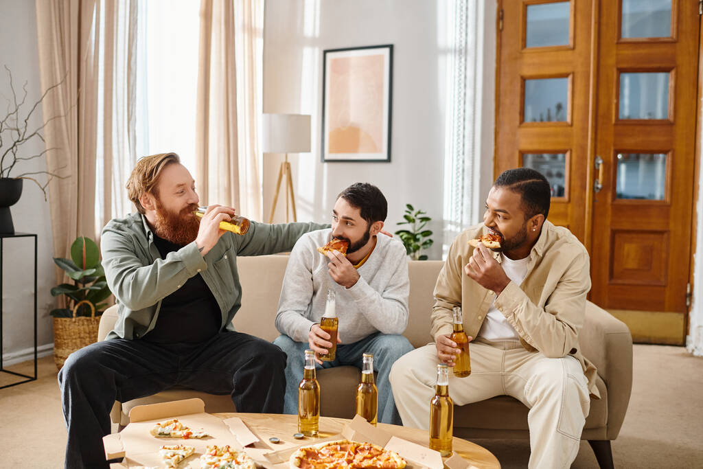 Trzech przystojnych, wesołych mężczyzn różnych ras siedzi na kanapie, jedząc pizzę i pijąc piwo, dzieląc się śmiechem i dobrymi czasami. - Zdjęcie, obraz