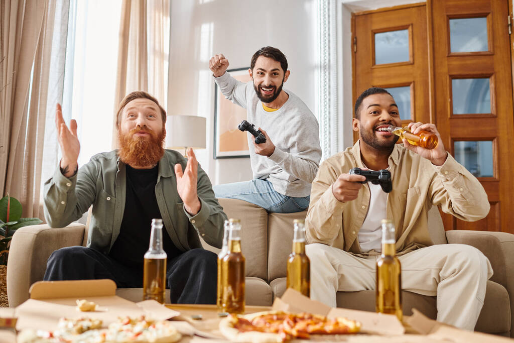 3つのハンサムで陽気な異なるレースの男性がテーブルの周りに座り,ピザと他の会社をカジュアルな設定で楽しんでいます. - 写真・画像