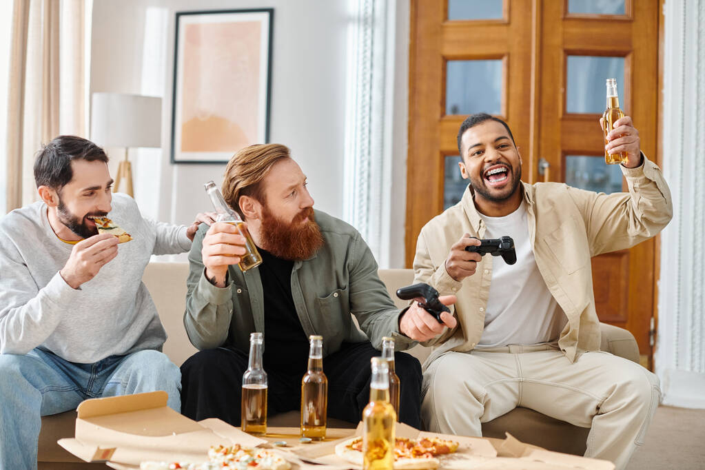 Три веселых, межрасовых мужчины в повседневной одежде сидеть на диване, наслаждаясь пиццей и пивом вместе. - Фото, изображение