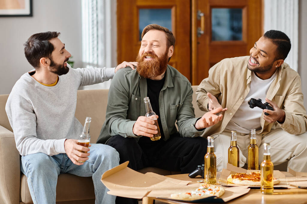 Tres hombres guapos y alegres de diferentes razas, en atuendo casual, disfrutando de las bebidas y la compañía de los demás en una mesa. - Foto, Imagen