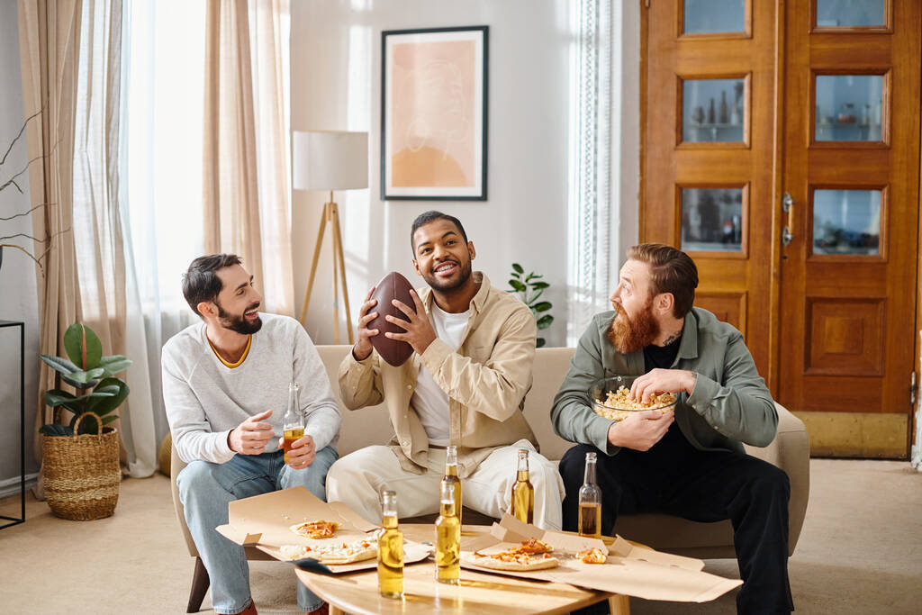 Három vidám, fajok közti férfi alkalmi öltözékben, akik együtt pizzáznak egy asztal körül, kényelmes környezetben.. - Fotó, kép