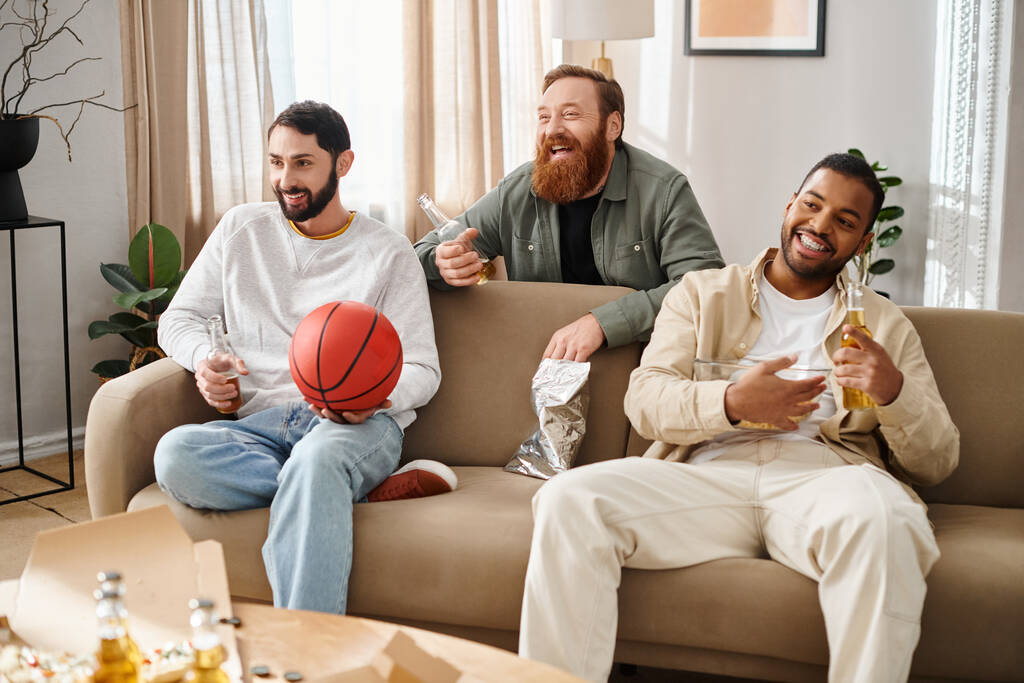 Trzech wesołych, międzyrasowych przyjaciół siedzi razem na kanapie w luźnym stroju, ciesząc się świetnym spędzaniem czasu w domu. - Zdjęcie, obraz