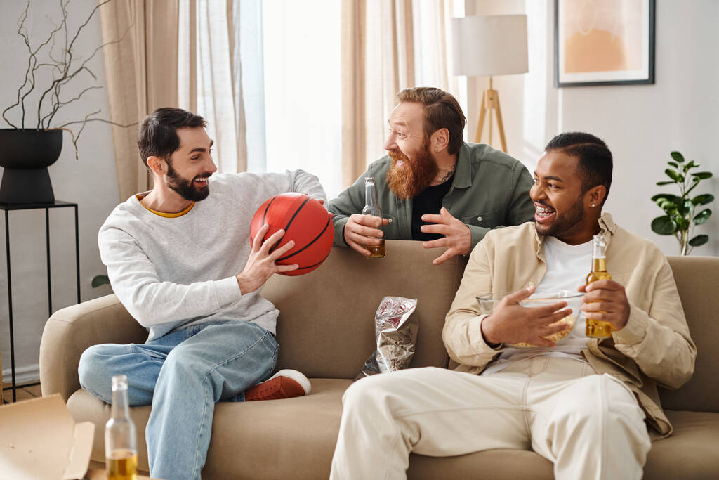 Três homens bonitos inter-raciais em trajes casuais ligando e rindo alegremente enquanto sentados em cima de um sofá. - Foto, Imagem