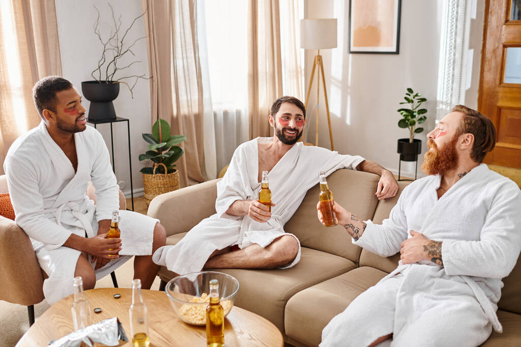 Drei bunt gemischte, gut gelaunte Männer in Bademänteln unterhalten sich auf einer Couch und lachen.. - Foto, Bild