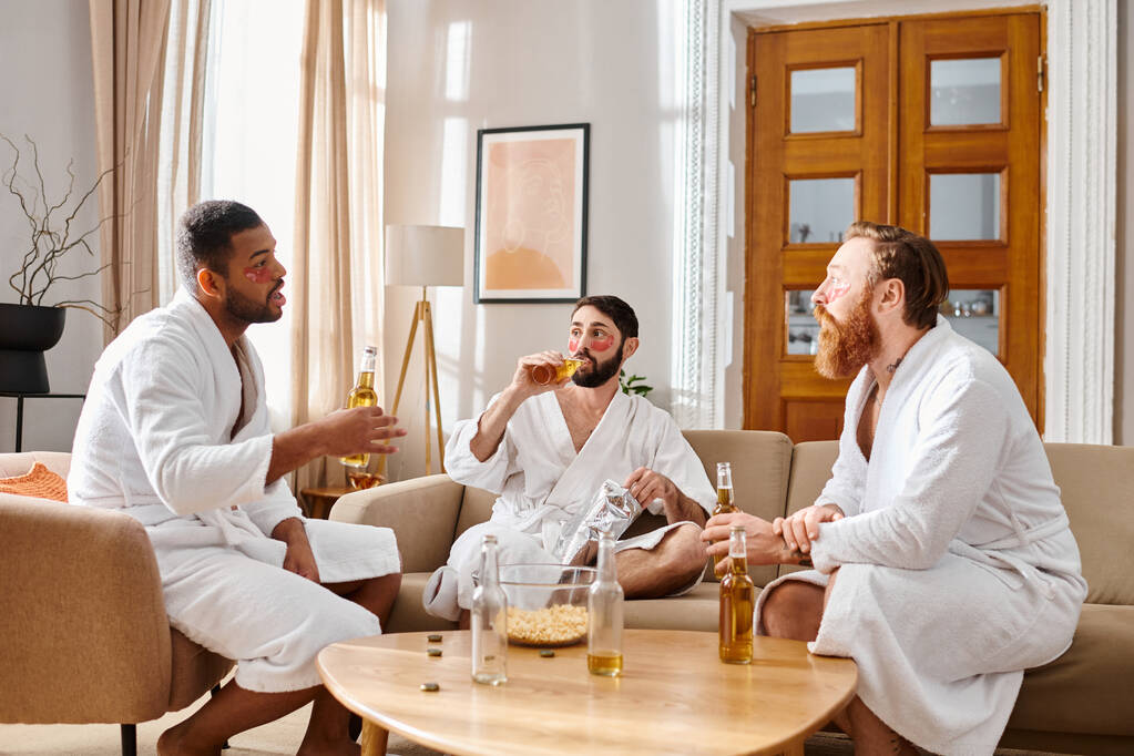 Három vidám férfi, különböző háttérrel, fürdőköpenyben, megosztják egymással a nevetésüket és bajtársiasságukat a nappali asztal körül.. - Fotó, kép