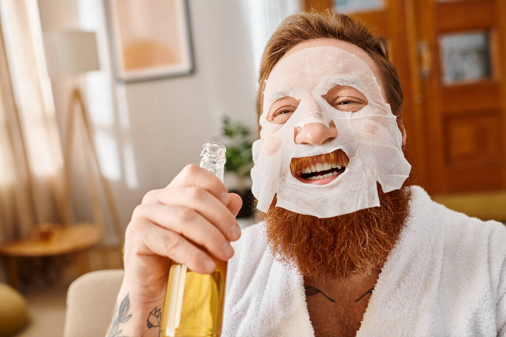 Un hombre con una máscara facial sostiene una botella de oso y sonríe felizmente. - Foto, imagen