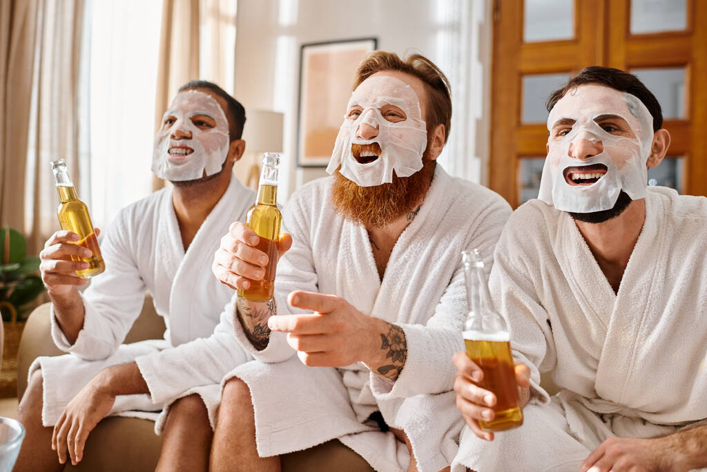 Tres hombres alegres, diversos en el fondo, usando máscaras faciales, albornoces, vinculación sobre la cerveza. - Foto, imagen