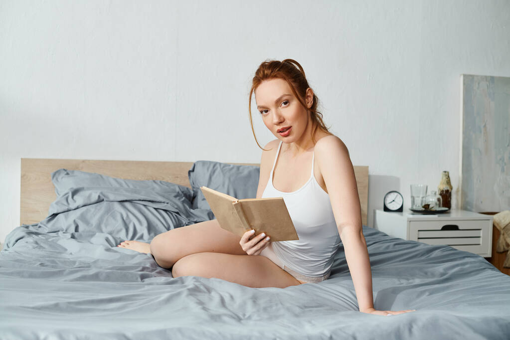Zarif giyinmiş bir kadın yatakta otururken huzur içinde kitap okuyor.. - Fotoğraf, Görsel