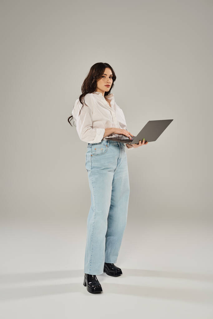 Plus velikost žena sebevědomě stojí, drží notebook ve stylovém oblečení na šedém pozadí. - Fotografie, Obrázek