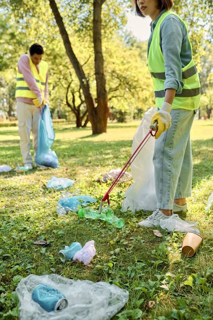 Социально активная любящая пара в защитных жилетах и перчатках вместе очищает парк под золотым солнцем. - Фото, изображение