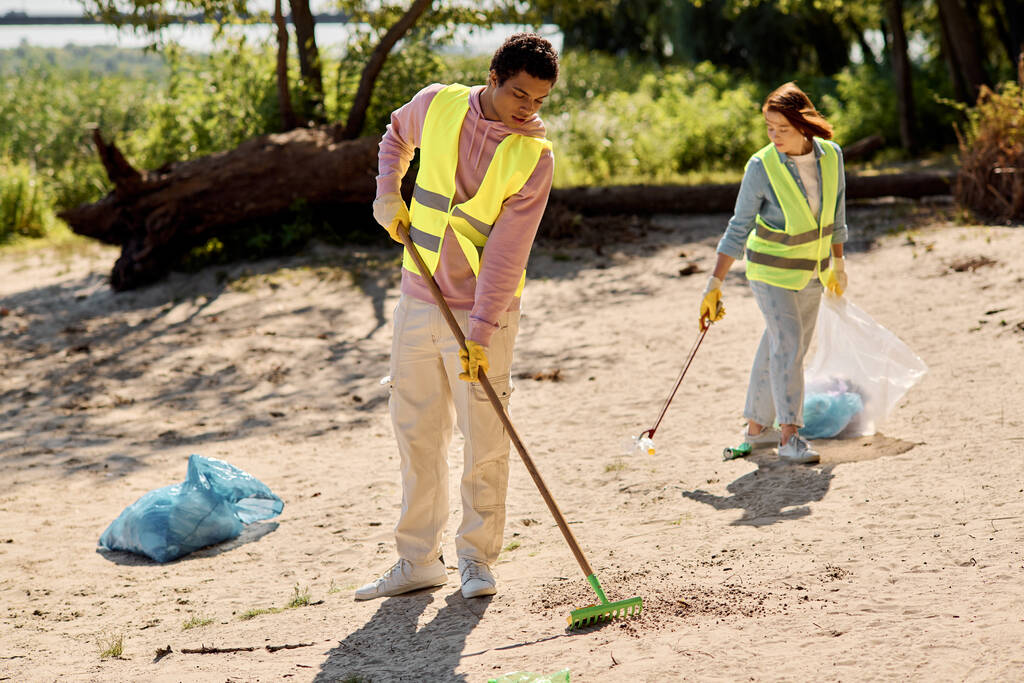 Een divers en liefdevol koppel, gehuld in veiligheidsvesten en handschoenen, staan in het zand, maken samen een park hartstochtelijk schoon. - Foto, afbeelding