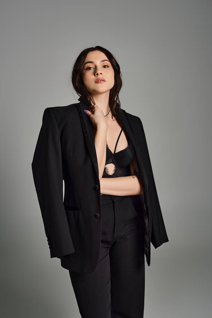 Uma bela mulher plus-size posa confiantemente em um terno preto elegante contra um pano de fundo cinza. - Foto, Imagem