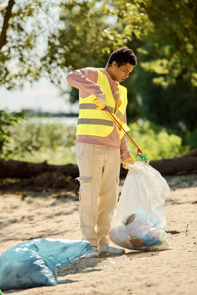 Мужчина стоит вдоль береговой линии, держа пластиковый пакет, размышляя о влиянии мусора на окружающую среду на наших пляжах. - Фото, изображение