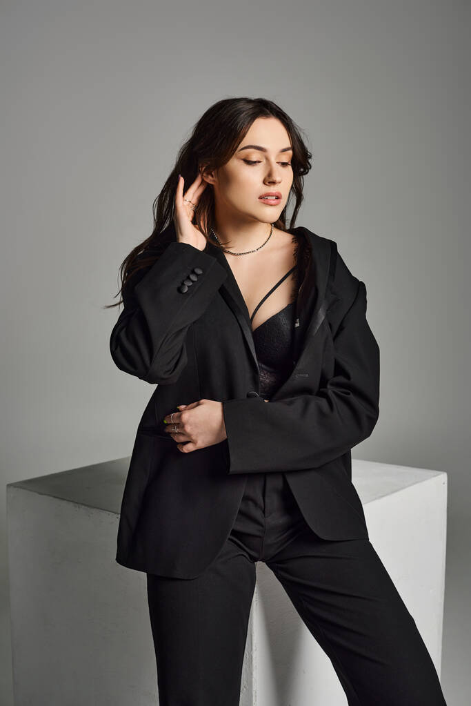 Além de mulher tamanho exalando confiança em um terno preto elegante marcando uma pose em um pano de fundo cinza. - Foto, Imagem