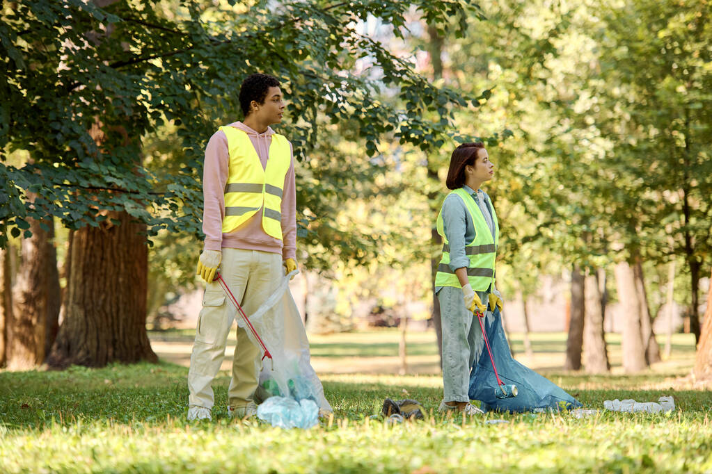 Una pareja socialmente activa y diversa en chalecos de seguridad y guantes que limpian el parque juntos. - Foto, Imagen