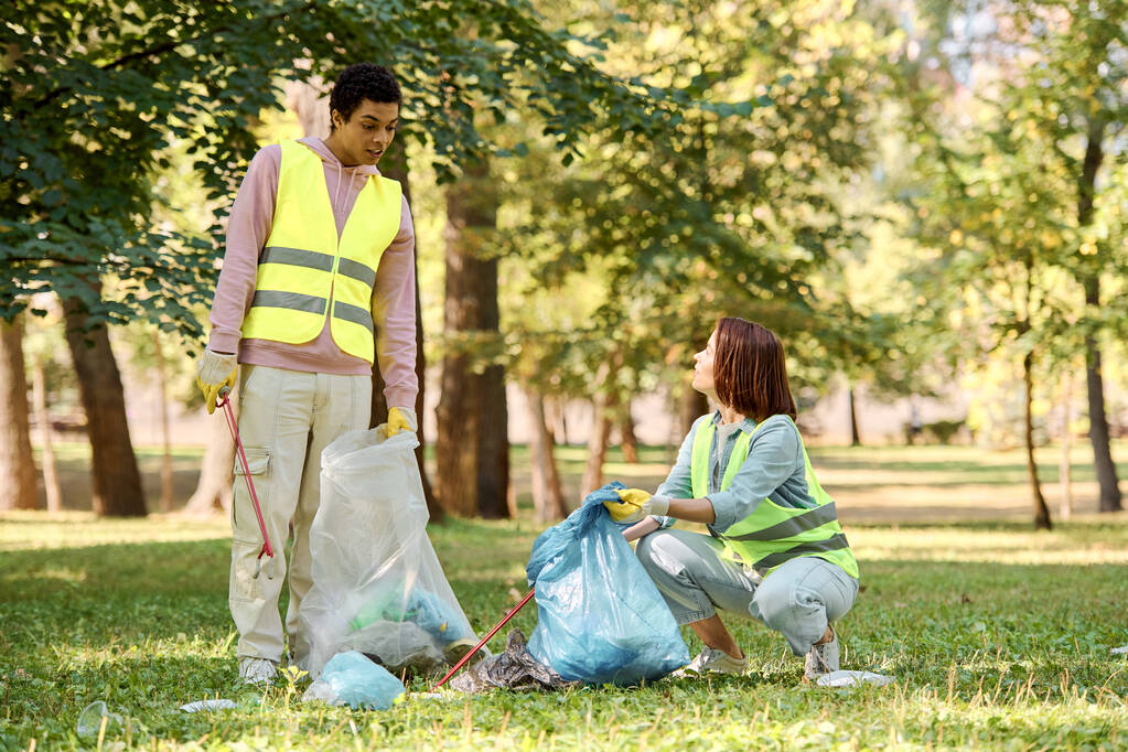 Una pareja amorosa diversa socialmente activa en chalecos de seguridad y guantes limpiando un parque juntos. - Foto, Imagen