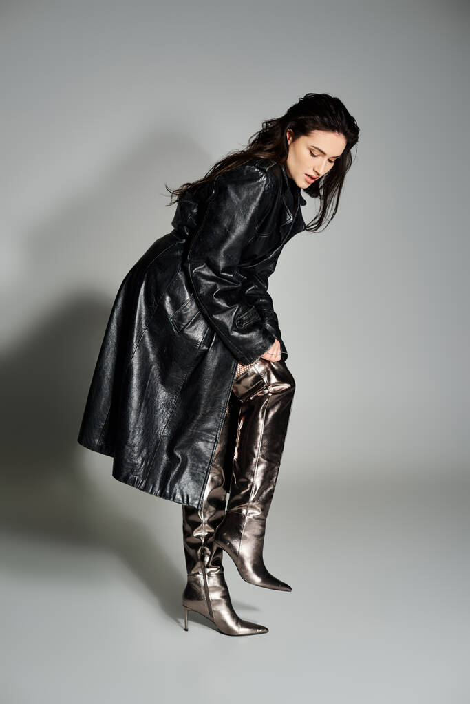 Una hermosa mujer de talla grande posa con un elegante abrigo negro y botas sobre un fondo gris. - Foto, imagen