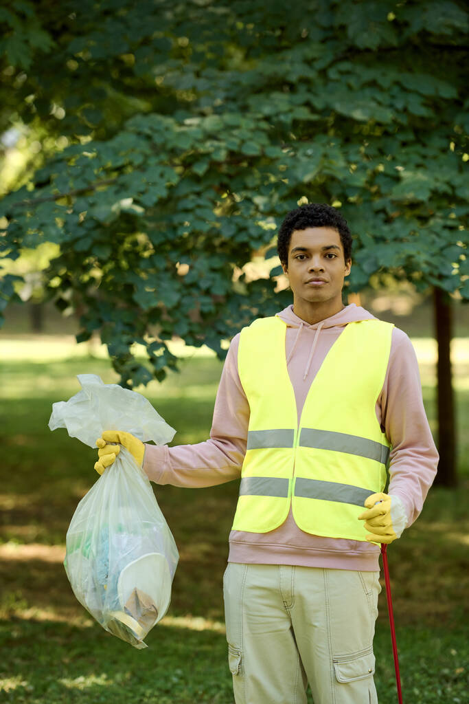 Αφροαμερικάνος με κίτρινο γιλέκο κρατώντας μια σακούλα σκουπιδιών.. - Φωτογραφία, εικόνα