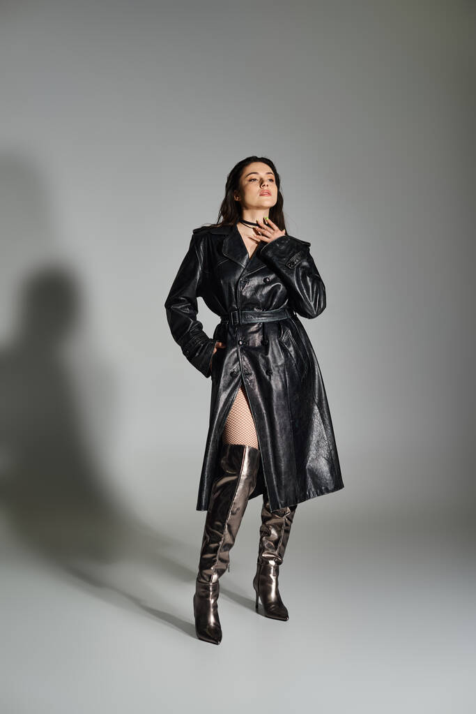 Стильный плюс размер женщина уверенно стоит в черном пальто и сапоги на сером фоне, источая элегантность. - Фото, изображение