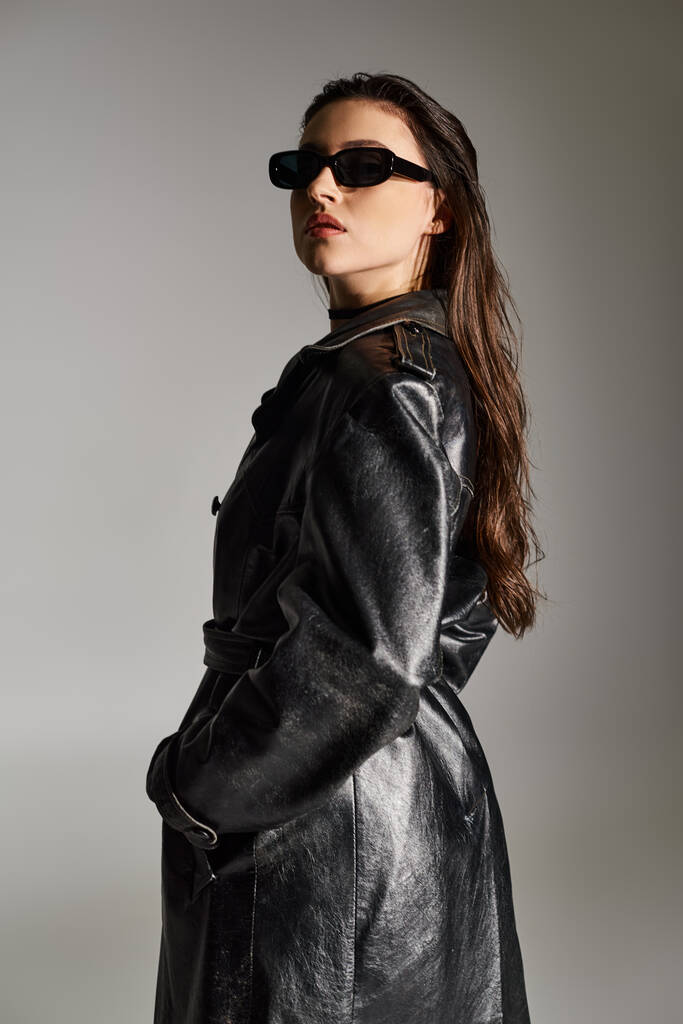 Жінка плюс розмір викриває стиль в чорному пальто і сонцезахисні окуляри на сірому тлі, вражаючи впевнену позу. - Фото, зображення