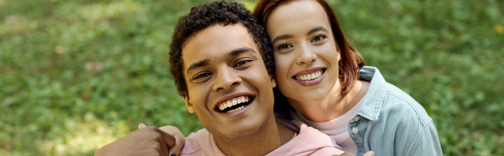 Un uomo e una donna, in abiti vivaci, condividono un momento gioioso mentre sorridono radiosamente per la fotocamera in un parco. - Foto, immagini