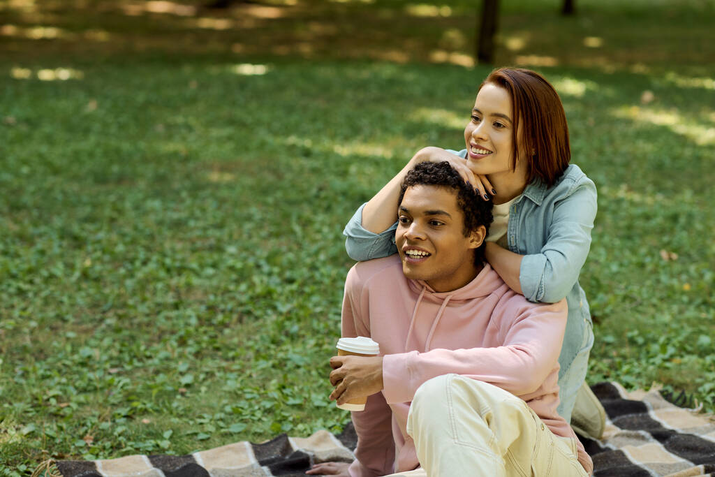 Una pareja, vestida vibrantemente, sentada sobre una manta en un parque, compartiendo un momento de unión en medio de una exuberante vegetación. - Foto, imagen