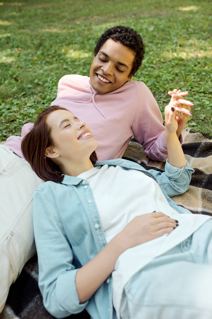 Un homme et une femme en tenue vibrante couchaient ensemble sur une couverture dans l'herbe, profitant d'un moment de détente dans le parc. - Photo, image
