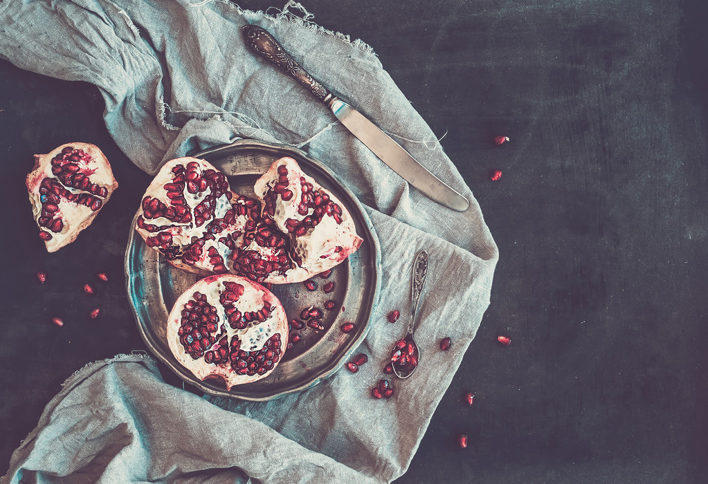 Червоний стиглий очищений гранат на сільській металевій тарілці та бежевий кухонний рушник на темному фоні
 - Фото, зображення