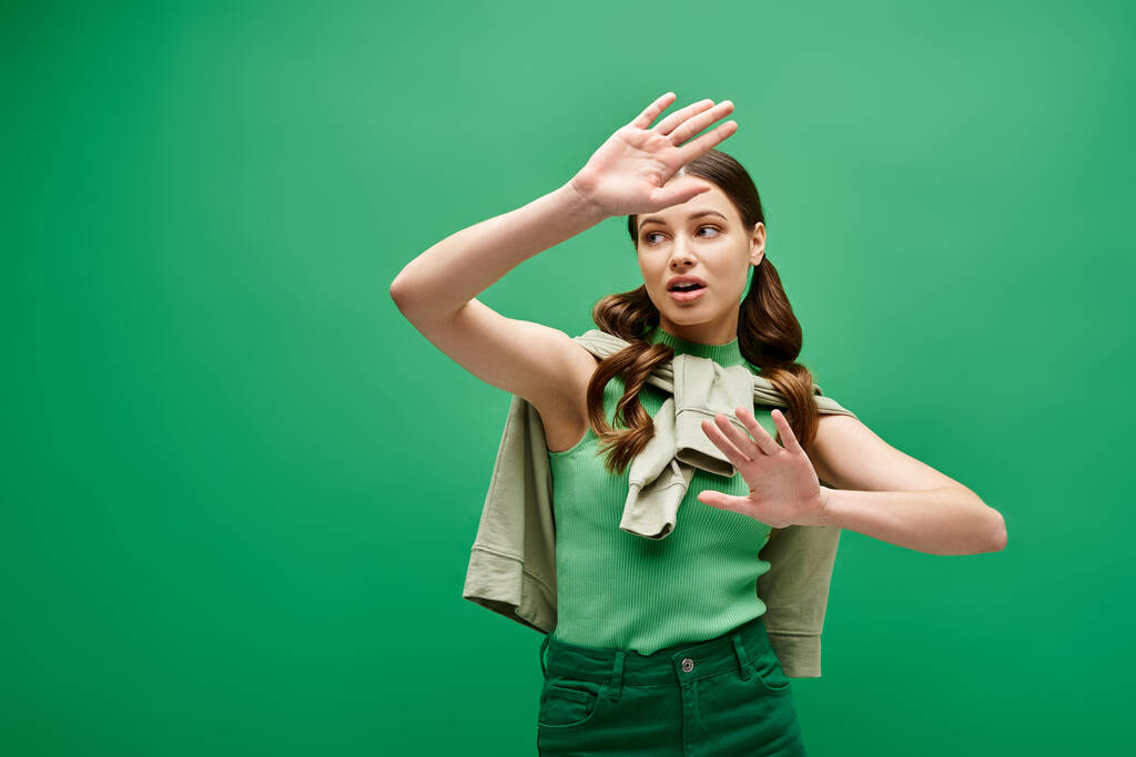 Egy húszas éveiben járó fiatal nő zöld ingben, kecsesen kézmozdulatot tesz egy stúdióban.. - Fotó, kép