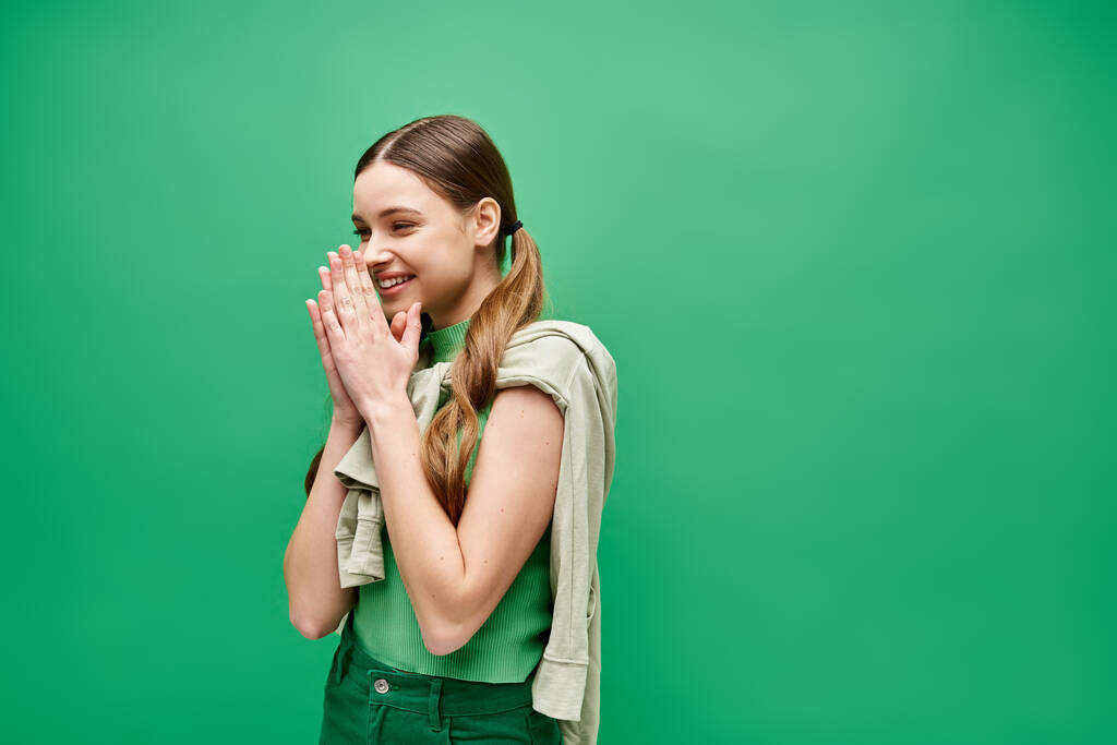 Μια ευτυχισμένη νεαρή γυναίκα στα 20 της στέκεται με αυτοπεποίθηση μπροστά σε ένα ζωντανό πράσινο φόντο σε ένα σκηνικό στούντιο.. - Φωτογραφία, εικόνα